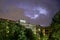 Buildings and green trees at night, illuminated sky during a lightning storm