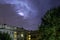 Buildings and green trees at night, illuminated sky during a lightning storm