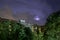 Buildings and green trees at night, illuminated sky during a lightning storm