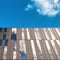 Buildings with wooden and glass mirror windows reflect the blue sky and white clouds.