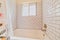 Built in bathtub inside bathroom with white tiles on wall and sliding window