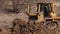 Bulldozer at construction site shovels soil into a heap. Powerful yellow earthmover crumbles sand