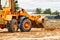 Bulldozer or loader moves the earth at the construction site against the blue sky. An earthmoving machine is leveling the site.