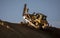 Bulldozer with a single shank ripper on a steep hill at cresting a ridge