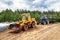 A bulldozer and a tractor compact the cut grass in a silage trench.