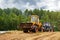 A bulldozer and a tractor compact the cut grass in a silage trench.