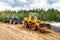 A bulldozer and a tractor compact the cut grass in a silage trench.