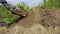 Bulldozer unloading soil from bucket at earth works with garden on background