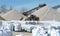 Bulldozer at work in a gravel pit between dunes and conveyor belts on one side and products packaged on the other