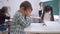 Bullying, tired schoolboy sits at a desk in classroom on background of classmates and female teacher near blackboard