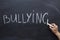 Bullying word handwritten on a chalkboard. Hand with chalk