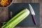 Bunch of celery washed and ready to chop on a black cutting board with chef knife