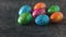 A bunch of colorful eggs scattered on a dark rustic table. The decoration of the Easter table.