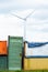 Bunch of colorful, rusty  metal cargo containers at metal scrap store. Wind energy windmill in background. Concept of recycling