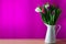 Bunch of colorful tulip flowers in jug in front of violet wall background. View with copy space.