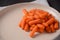 Bunch of cooked small boiled carrots on white plate.