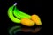 A bunch of fresh tropical green bananas and a pair of ripped mangoes on dark background