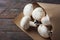 Bunch of freshly picked white button mushrooms in brown Kraft paper bag on rustic wood table