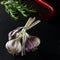 A bunch of garlic on a black background next to the rormarin and chili peppers