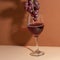 Bunch of grapes above the wineglass with red wine isolated on beige background. Alcohol drink. Festive mood