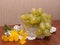 A bunch of grapes in a glass vase.Vase and dandelions on a knitted napkin.