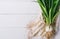 Bunch of green young scallions with roots on a white background of old wooden boards vintage top view, healthy diet food