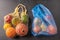 Bunch of mixed organic fruit, vegetables and greens in a string bag and plastic on dark background. Zero waste add