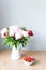 Bunch of Pink peonies in vase and strawberry on the wooden table . Flowers on a beige wooden table near the window. Home