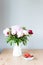 Bunch of Pink peonies in vase and strawberry on the wooden table . Flowers on a beige wooden table near the window. Home
