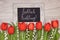 Bunch of red tulips and lily of the valley flowers on light wood with black board