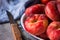 Bunch of ripe organic colorful red saturn peaches with water drops on white plate, knife, blue napkin, dark kitchen table