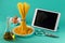 Bunch of spaghetti standing upright on a bright colored background surrounded by tablet computer, chicken eggs, olive