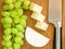 Bunch of sweet green grapes, pieces of tasty cheese camembert and chef knife on a brown wooden cutting board. Soft cheese covered