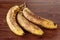 Bunch of three rotten, spotted bananas on a brown wooden surface