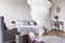 Bunch of white balloons in the middle of classy grey bedroom with elegant dresser with golden mirror, copy space on the empty wall