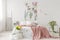 A bunch of yellow fresh cut flowers in a bright bedroom interior with a bed dressed in white linen and peach blanket. Fabric on th