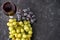 Bunches of ripe green and blue grapes with a glass of red wine, a corkscrew and wine corks on a dark stone background. Top view.