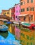 Burano island picturesque street with small colored houses, tourists on wooden bridge and beautiful water reflections