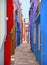 Burano island picturesque very narrow street and courtyard with small colorful houses in row against cloudy blue sky, Venice Italy