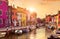 Burano island in Venice Italy picturesque sunset over canal with boats among old colourful houses stone streets.