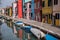Burano, Italy. Typical street scene showing brightly painted houses reflected in the canal, with boats.
