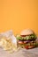 Burger with beef, tomato, cheese, lettuce and potato chips on wooden counter. Yellow background.