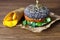 Burger with the black bun, on the kraft paper with fried potatoes on brown wooden background