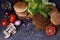 Burger ingredients: beef patties, sesame bun, fresh vegetables, pepper, mushrooms over dark wooden table.