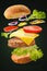Burger levitating on a black background with beef cutlet, vegetables, cheese and sauce and mustard on a bun with sesame