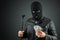 Burglar, a thug in a balaclava holds dollars in his hands on a dark background. Robbery, hacker, crime, theft. Copy space