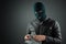 Burglar, a thug in a balaclava holds dollars in his hands on a dark background. Robbery, hacker, crime, theft. Copy space