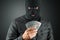 Burglar, a thug in a balaclava holds dollars in his hands on a dark background. Robbery, hacker, crime, theft. Copy space