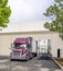 Burgundy big rig semi truck with refrigerator semi trailer going into the warehouse door for loading cargo for delivery