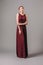 Burgundy chic gown. Red cocktail sleeveless dress with rounded neckline. Relaxed young ginger lady. Studio shot. Bridesmaid`s mini